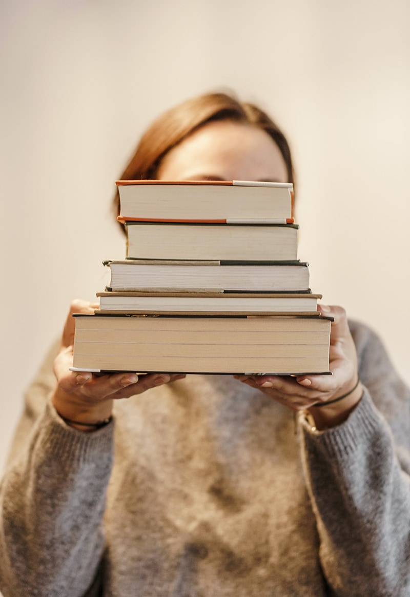 Frau hält Bücherstapel hoch