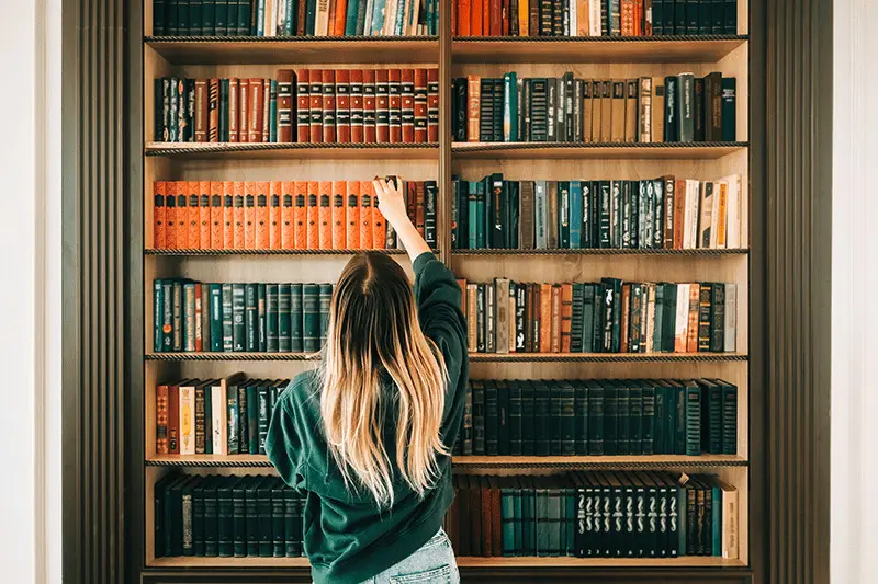 Frau nimmt ein Buch aus einem Bücherregal